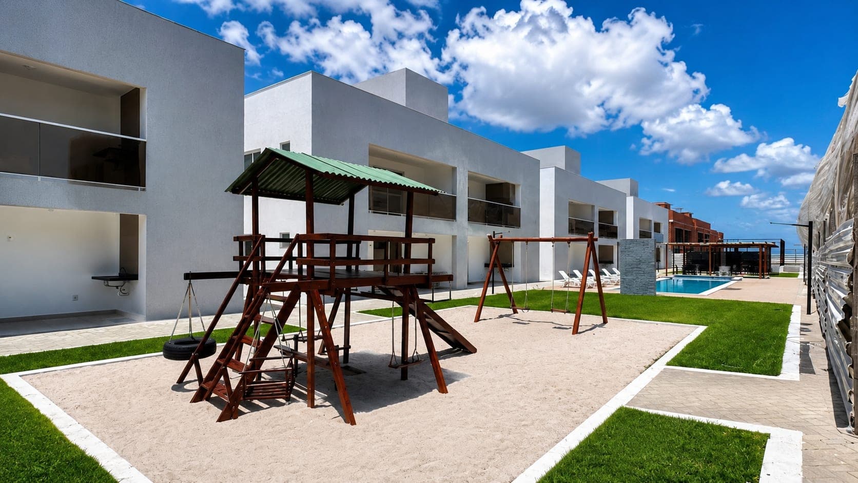 Parque infantil de madeira em área de areia entre os blocos do Visual Residence