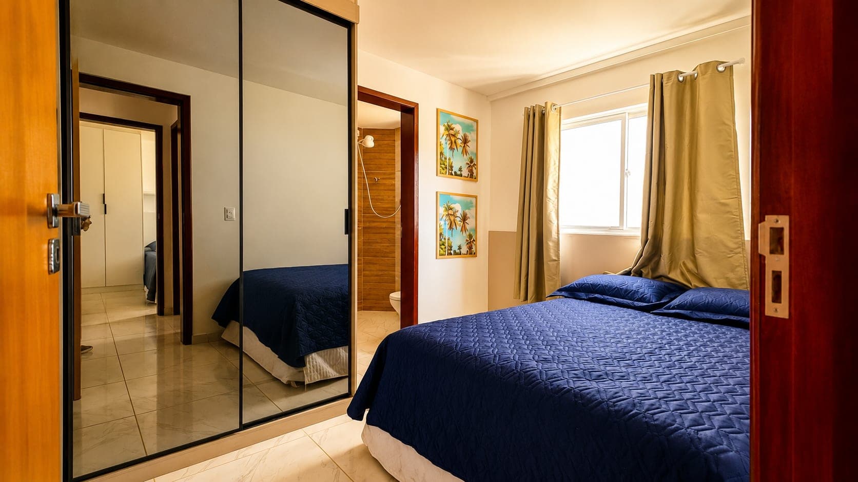 Suíte com cama de casal, guarda-roupa espelhado e banheiro privativo no Visual Residence